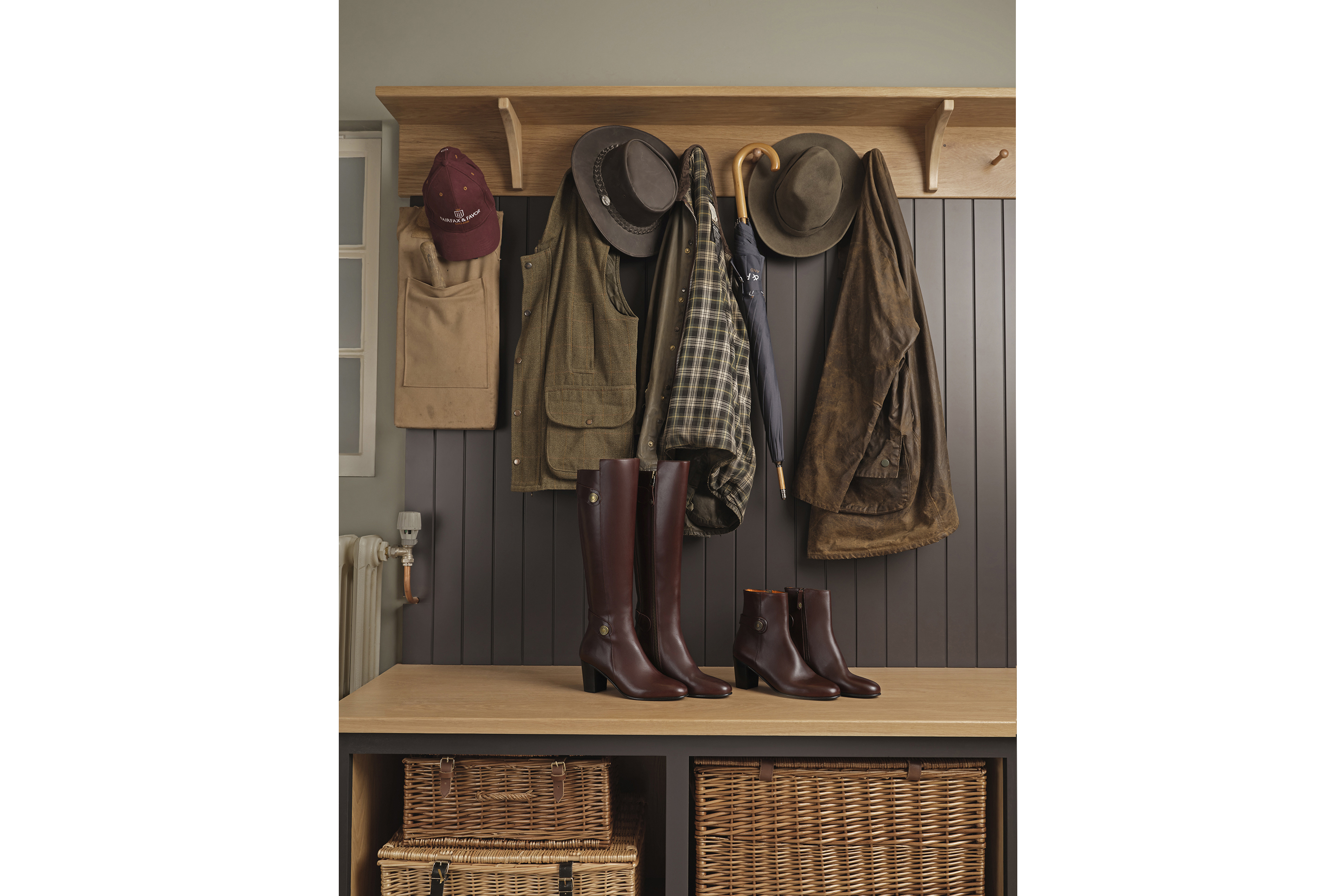 Brown leather boots sitting in front of coats and a umbrellas in a farmers countryside coat room